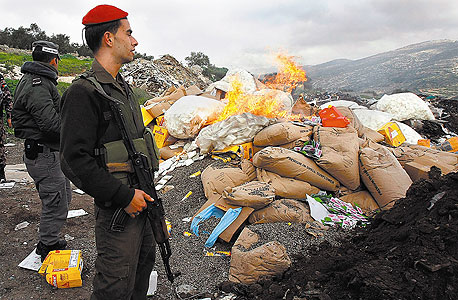 איש ביטחון פלסטיני ליד ערימה של מוצרים שרופים מההתנחלויות