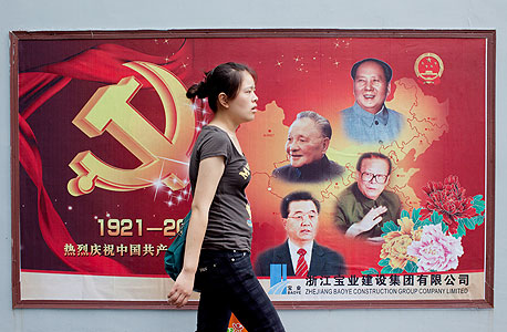 צעירה סינית בשנגחאי על רקע פוסטר המציין 90 שנה למפלגה הקומוניסטית. נציגיה ממשיכים לשלוט בעולם העסקים