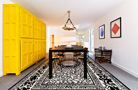 פינת האוכל בחלל המרכזי של הווילה. כוללת ארון קיר צהוב, שולחן, מנורה ושטיח פנתיאון בעיצוב סטודיו ג