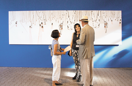האמנית מרב שין בן־אלון עם שניים מהמבקרים בתערוכה. ברקע ציור שלה ובו היער שמשפחתה ברחה אליו בזמן השואה