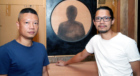 יופאן (משמאל) ויוג'ון צ'ן על רקע אחת העבודות במוזיאון פתח תקווה. "העץ הוא העצמות של העבודה והספרים הם השרירים שלה"