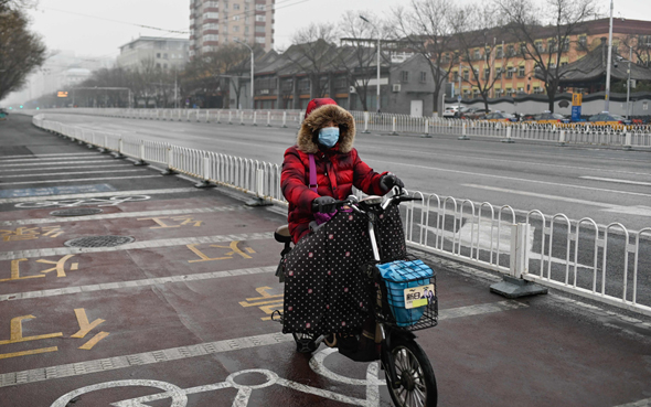 אישה רוכבת על אופניים עם מסיכה בבייג'ינג