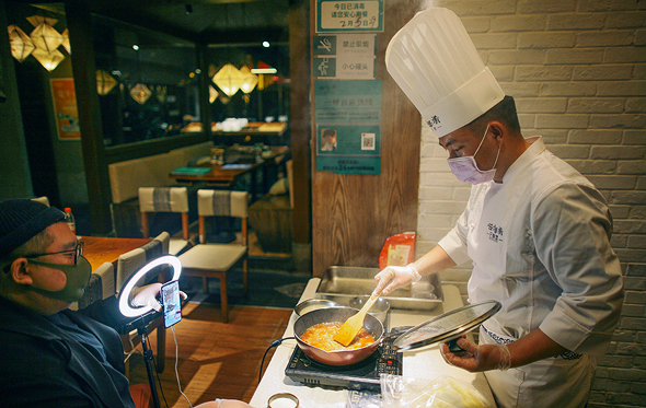 שף עטוי מסכה בעיר טיניאן בסין מעביר שיעור בישול מקוון במסעדה הריקה. המילניאלז שנאלצו לוותר על משלוחי מזון, החלו ללמוד לבשל, צילום: רויטרס