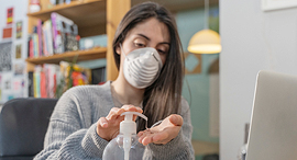 A woman using a hand sanitizer and wearing a mask. Photo: Shutterstock