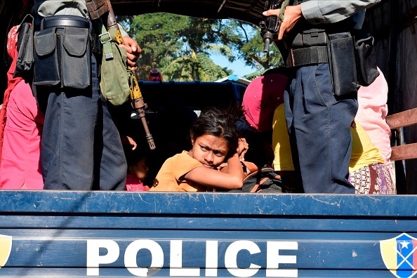 שוטר ב מיאנמר מלווה ילדה בת רוהינגה למחנה שלה לאחר שניסתה לברוח מהמדינה