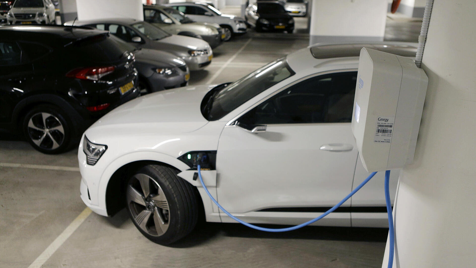 רכב אאודי לבן חשמלי ב טעינה ב חניון בניין משותף מכונית חשמלית 
