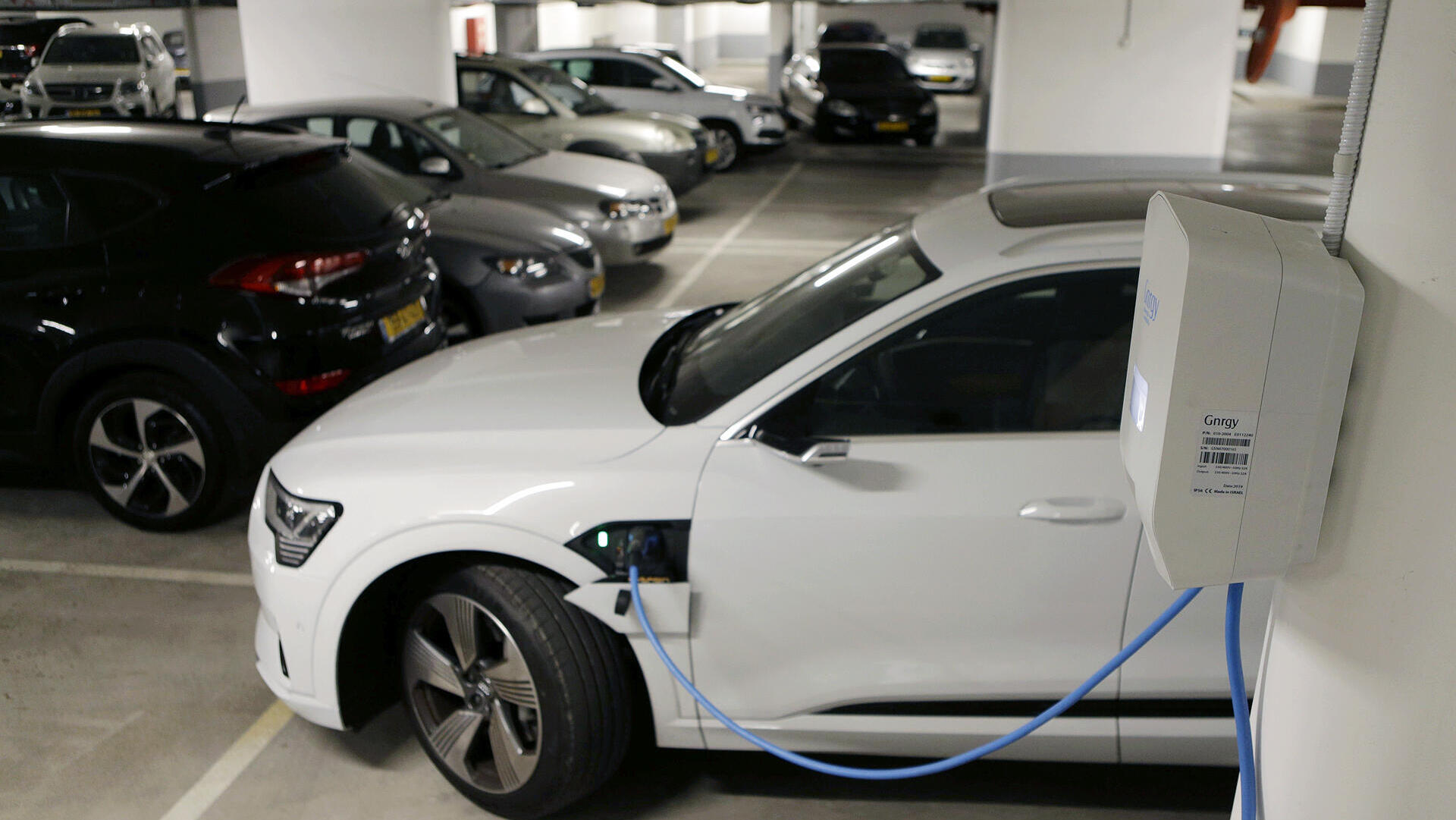 רכב אאודי לבן חשמלי ב טעינה ב חניון בניין משותף מכונית חשמלית 