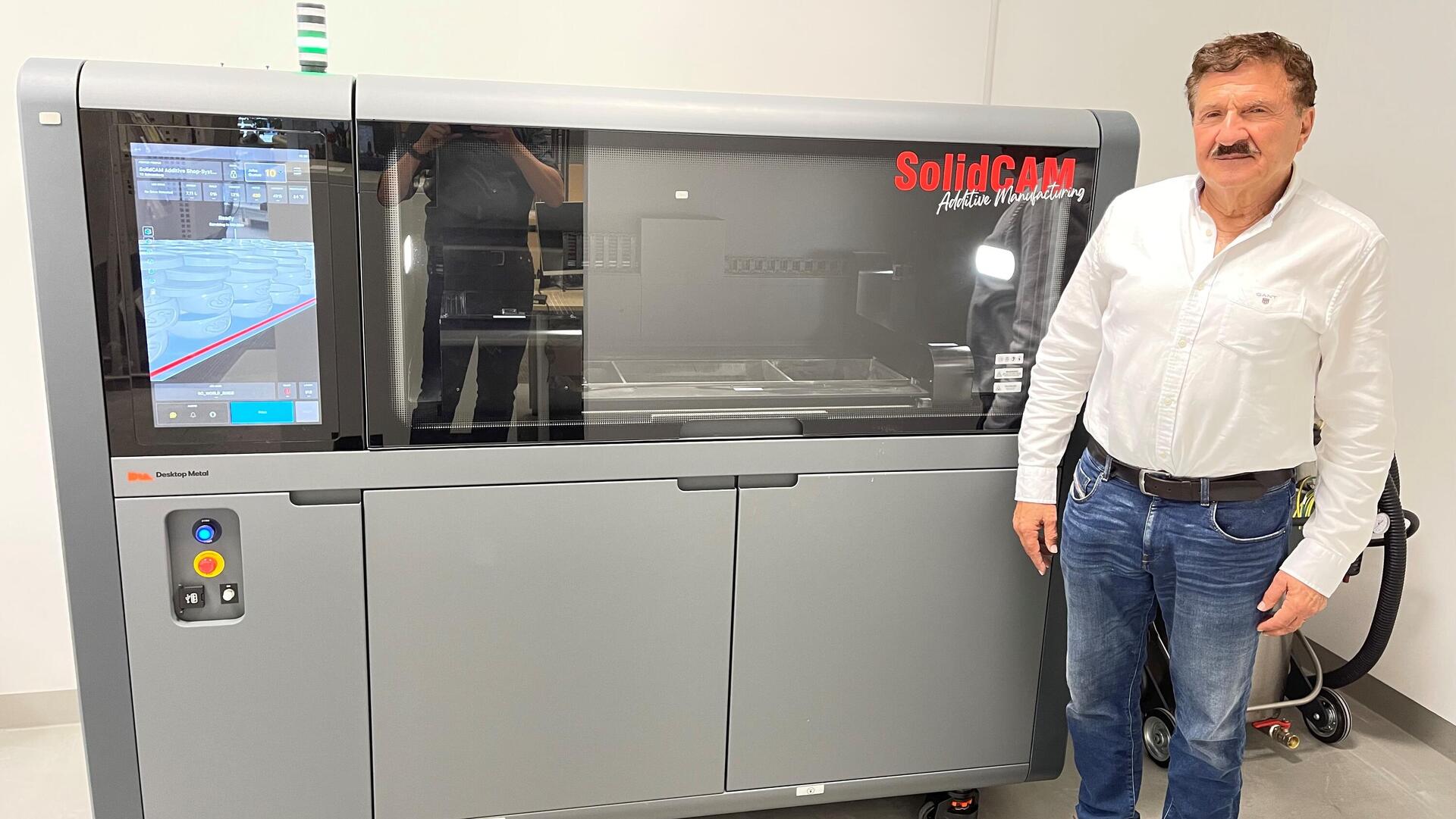 Dr. Emil Somekh stands next to a Desktop Metal Shop system, at the SolidCAM technology center in Germany 