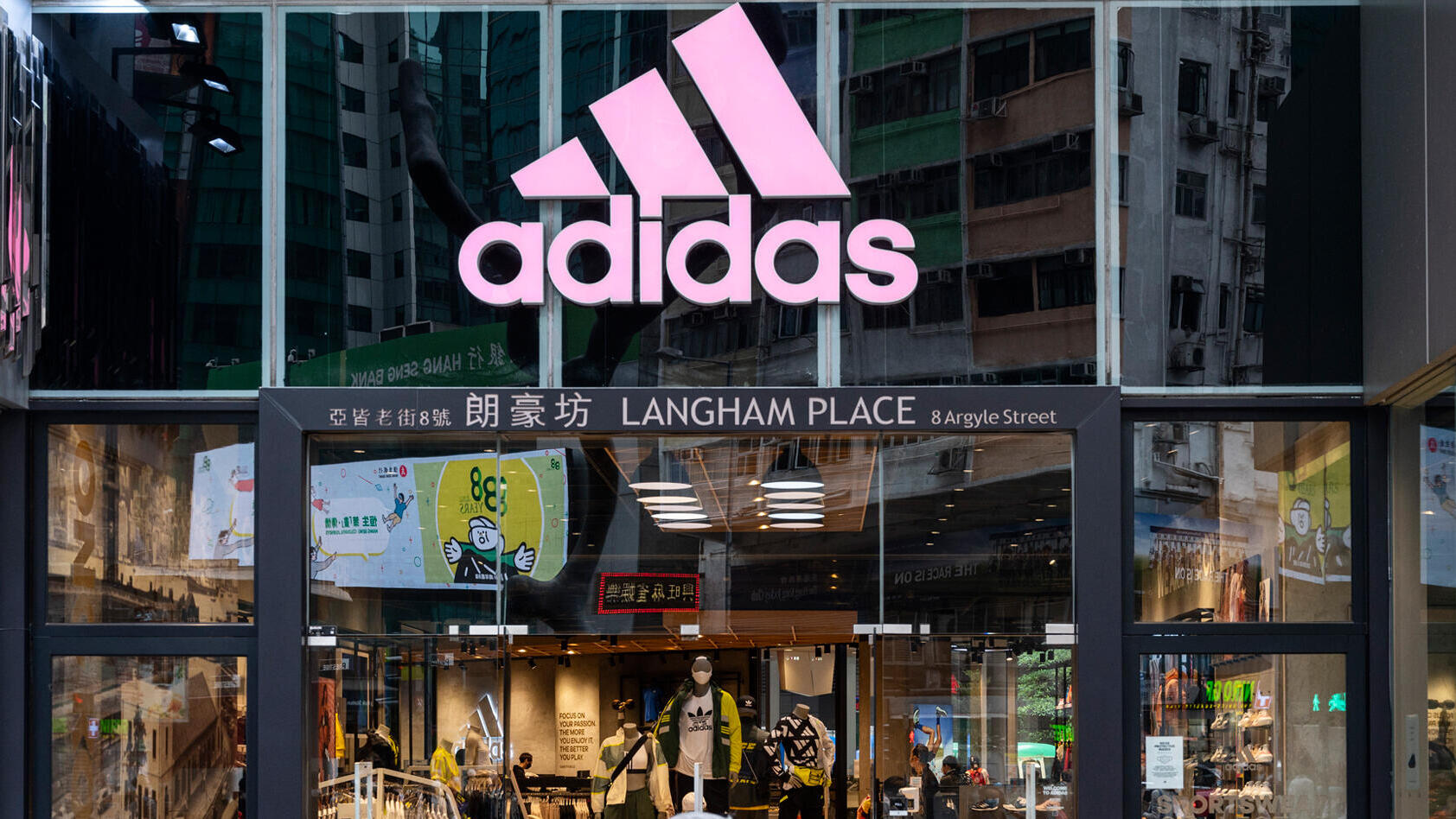 הולכי רגל חולפים על פני החנות והלוגו של מותג בגדי הספורט הרב-לאומי הגרמני אדידס בהונג קונג.