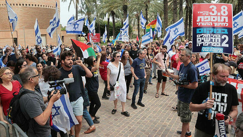 מפגינים עם שלטי מחאה ו דגלי ישראל ו אשף דגלי פלסטין מוחים ב אוניברסיטת תל אביב