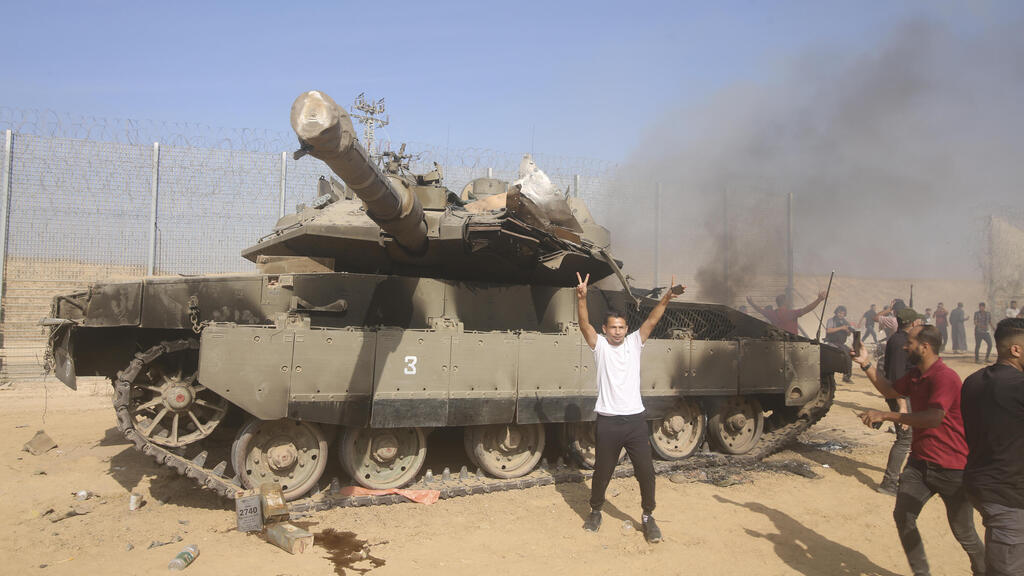 פלסטינים חוגגים לצד טנק ישראלי שרוף ב גבול עזה 7.10.23 (צילום: AP Photo/Hatem Ali) פלסטינים חוגגים לצד טנק ישראלי שרוף ב גבול עזה 7.10.23