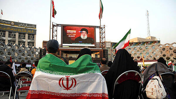 זוג תומכי חיזבאללה עם דגל איראן מאזין לנאומו של נסראללה בכיכר בטהרן