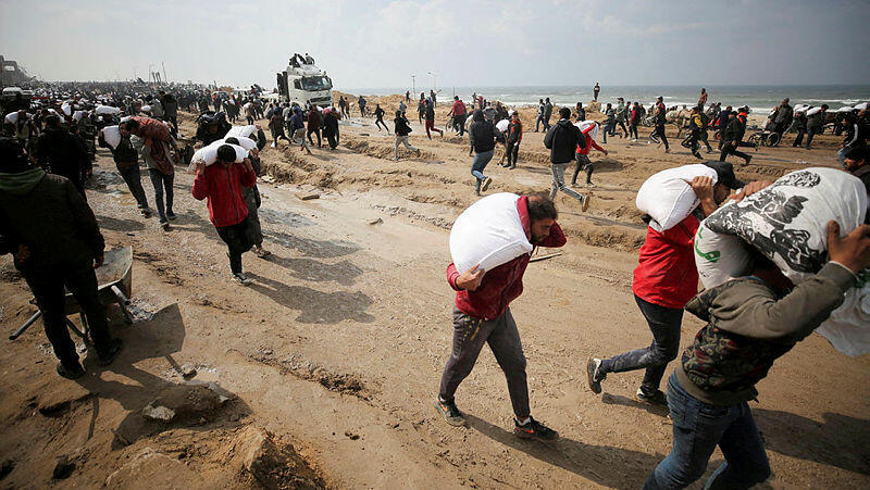 תושבים ב רצועת עזה נושאים שקי קמח שהובאו ב משאיות סיוע הומניטרי מלחמה בעזה 