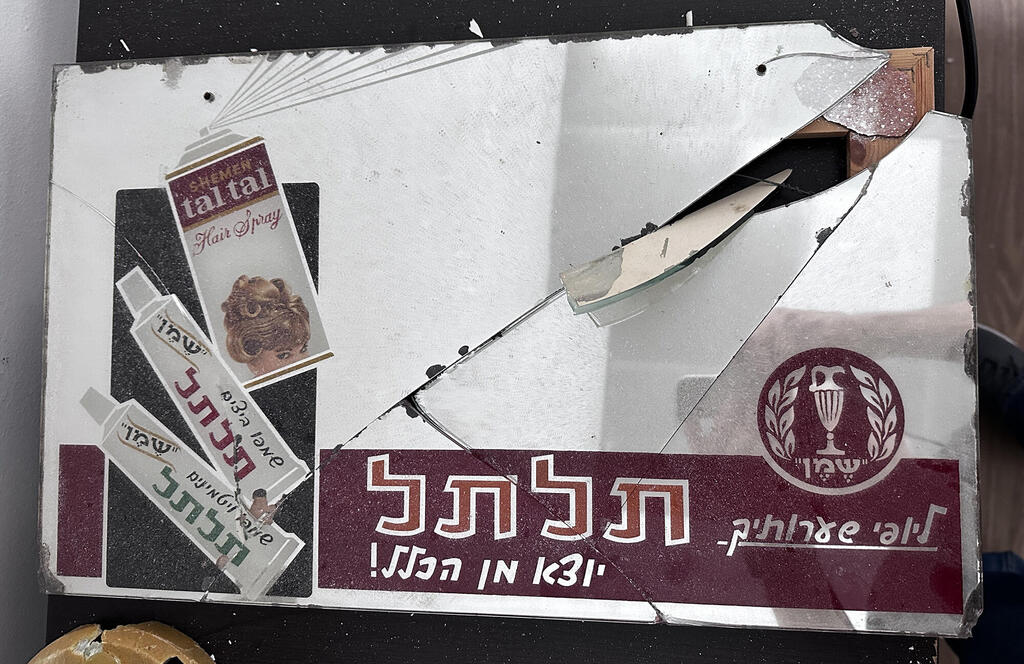 פריטים מהאוסף של הדי אור פרסומת מודפסת על גבי מראה משנות הששים שניזוקה בפגיעת הטיל פנאי