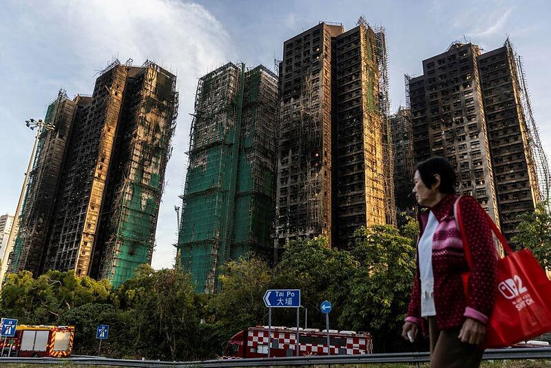 אישה חולפת על פני הבניינים שנפגעו בשריפה בהונג קונג (צילום: Isaac Lawrence / Getty Images AsiaPac) אישה חולפת על פני הבניינים שנפגעו בשריפה בהונג קונג