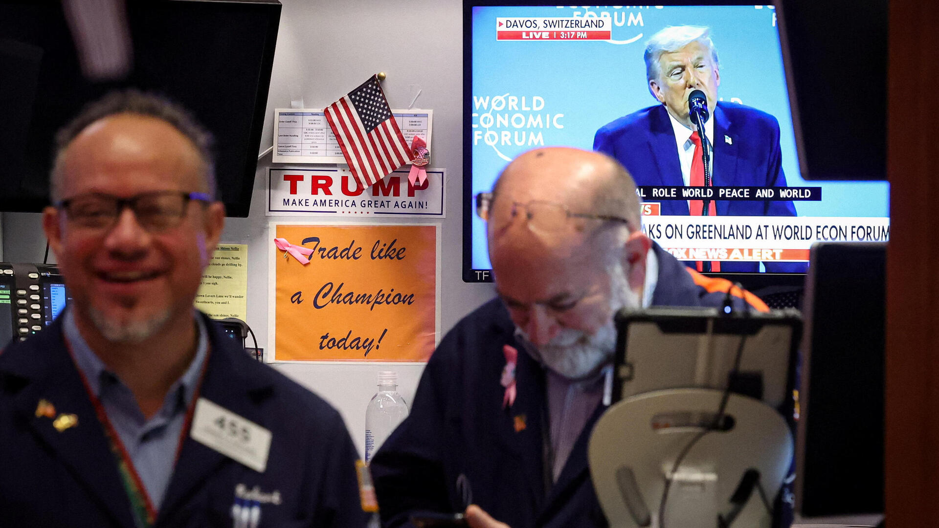 סוחרים ב בורסת ניו יורק על רקע טלוויזיה בה מוקרן נאום דונלד טראמפ ב פורום הכלכלי העולמי ב דאבוס 21.1.26